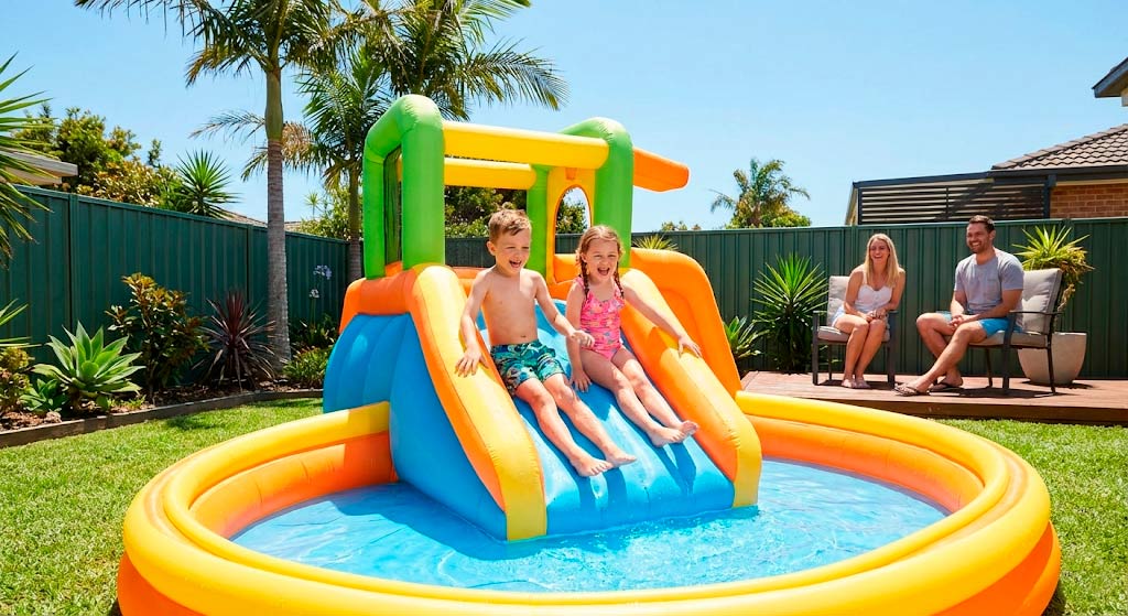 Счастливые дети играют в надувном игровом центре Intex с бассейном и горкой во дворе частного дома, родители наблюдают за безопасной игрой малышей в летний солнечный день